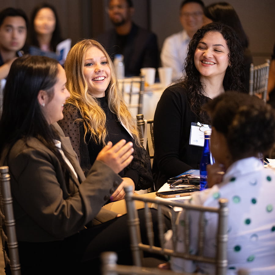 3 students sitting at a table in business casual attire laughing and conversing at BEST Boston