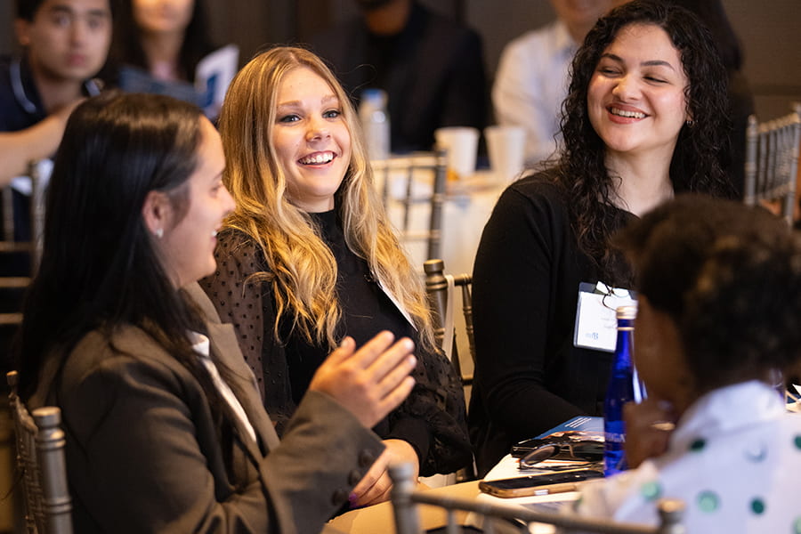 Group of students at a table at a reception in business casual attire.