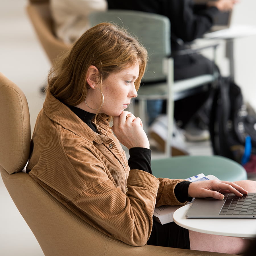 red headed student sideview contemplatively looks at computer with hand to chin